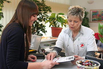 Foto: Frau wird von einer DRK-Mitarbeiterin bei der Blutspende  empfangen.